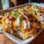 A spoonful of creamy Mississippi Mud Potatoes topped with melted cheddar, bacon bits, sour cream drizzle, and green onions.