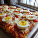 Close-up of a freshly baked Monster Eyeball Pizza topped with slices of hard-boiled eggs resembling eyeballs, cheese, and herbs.