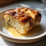 Close-up of a square serving of moist Overnight French Toast drizzled with golden syrup on a small plate.