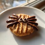 A single Peanut Butter Spider Cookie decorated with chocolate legs and candy eyes, sitting on a white plate.