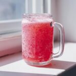 Close-up of a vibrant, fizzy Pink Witch Punch served in a clear glass mason jar mug, sitting on a sunlit windowsill.