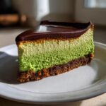 A slice of layered Polyjuice Potion Cheesecake featuring a dark crust, green and pale green filling, topped with shiny chocolate ganache.