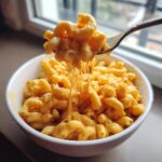 A fork lifting creamy Pumpkin Ale Mac And Cheese from a white bowl, showing a dramatic cheese pull.