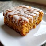 Close-up of a moist slice of Pumpkin Spice Latte Bars topped with white drizzle icing on a white plate.