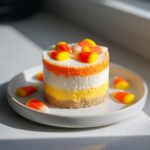 A single, layered Candy Corn Cheesecakes dessert topped with candy corn pieces on a white plate.