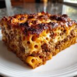 A close-up slice of rich Egyptian Goulash featuring tubular pasta, seasoned ground meat, and a deeply browned, cheesy top layer.