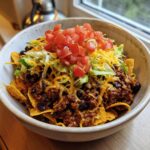 A close-up of Smothered Fritos Taco Bowls topped with seasoned ground beef, black beans, shredded cheese, lettuce, and diced tomatoes.