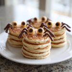 Close-up of three stacks of fun Spider Pancakes decorated with candy eyes and chocolate legs.