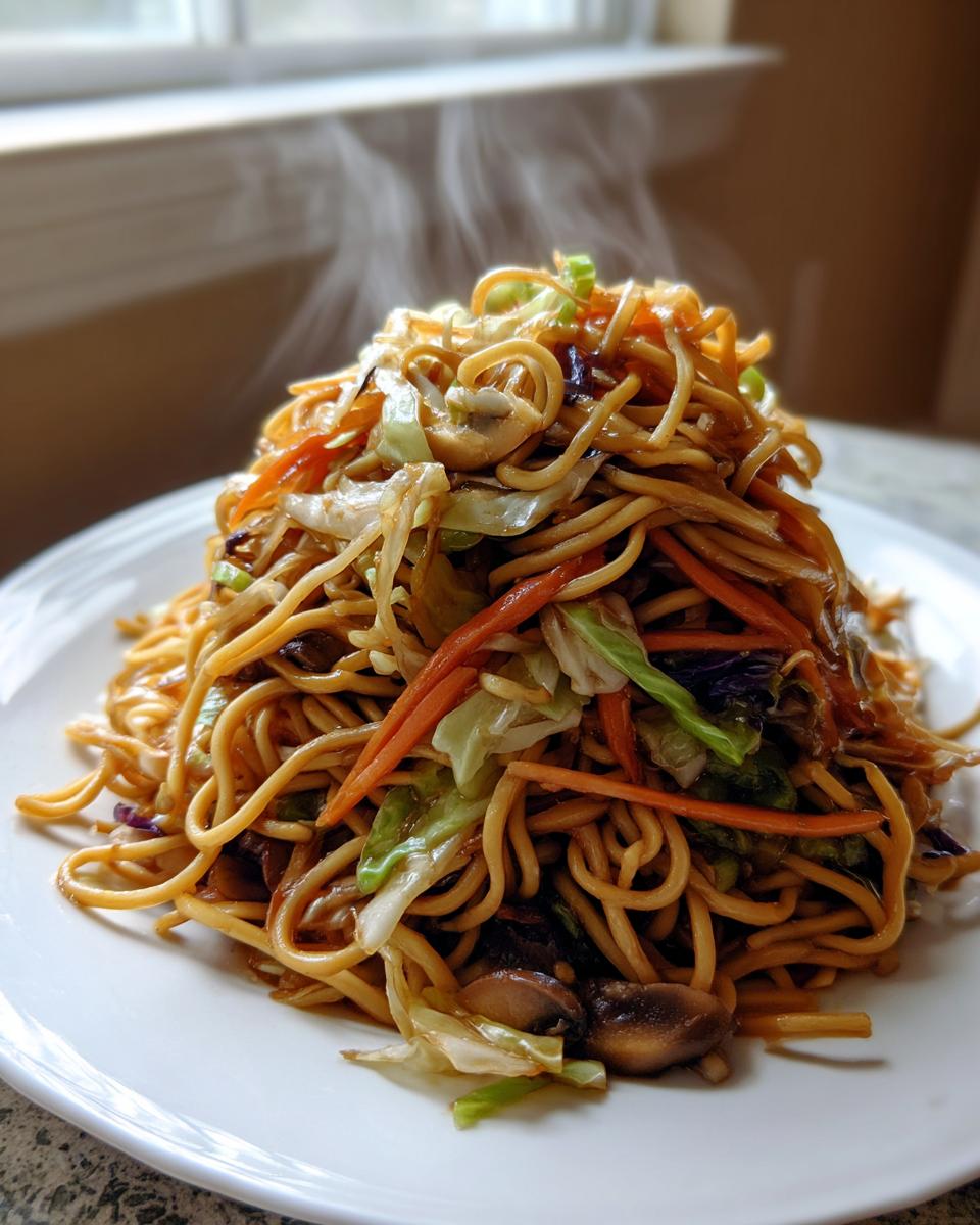 A tall mound of steaming hot Vegetarian Chow Mein noodles mixed with carrots, cabbage, and mushrooms on a white plate.