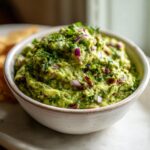 Close-up of a bowl of chunky Swamp Guacamole topped with fresh cilantro and diced red onion.