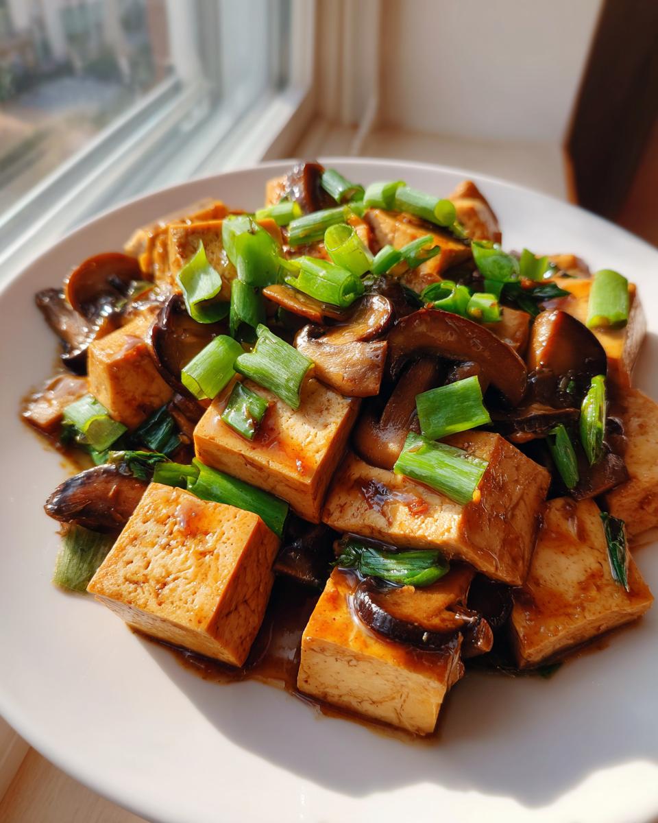 Close-up of golden brown tofu cubes and sliced mushrooms coated in sauce, garnished with bright green onions, ready for Tofu Mushroom Stir Fry.