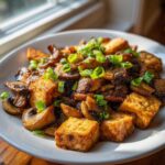 Close-up of crispy, golden Tofu Mushroom Stir Fry topped with fresh sliced green onions.