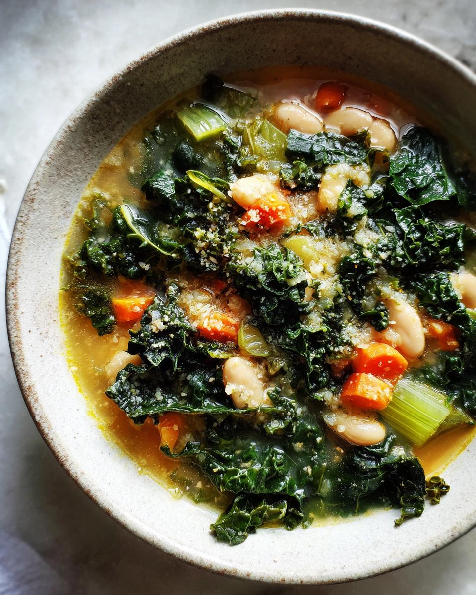 Close-up overhead shot of a bowl of White Bean Kale Soup, featuring dark green kale, white beans, carrots, and a sprinkle of cheese.