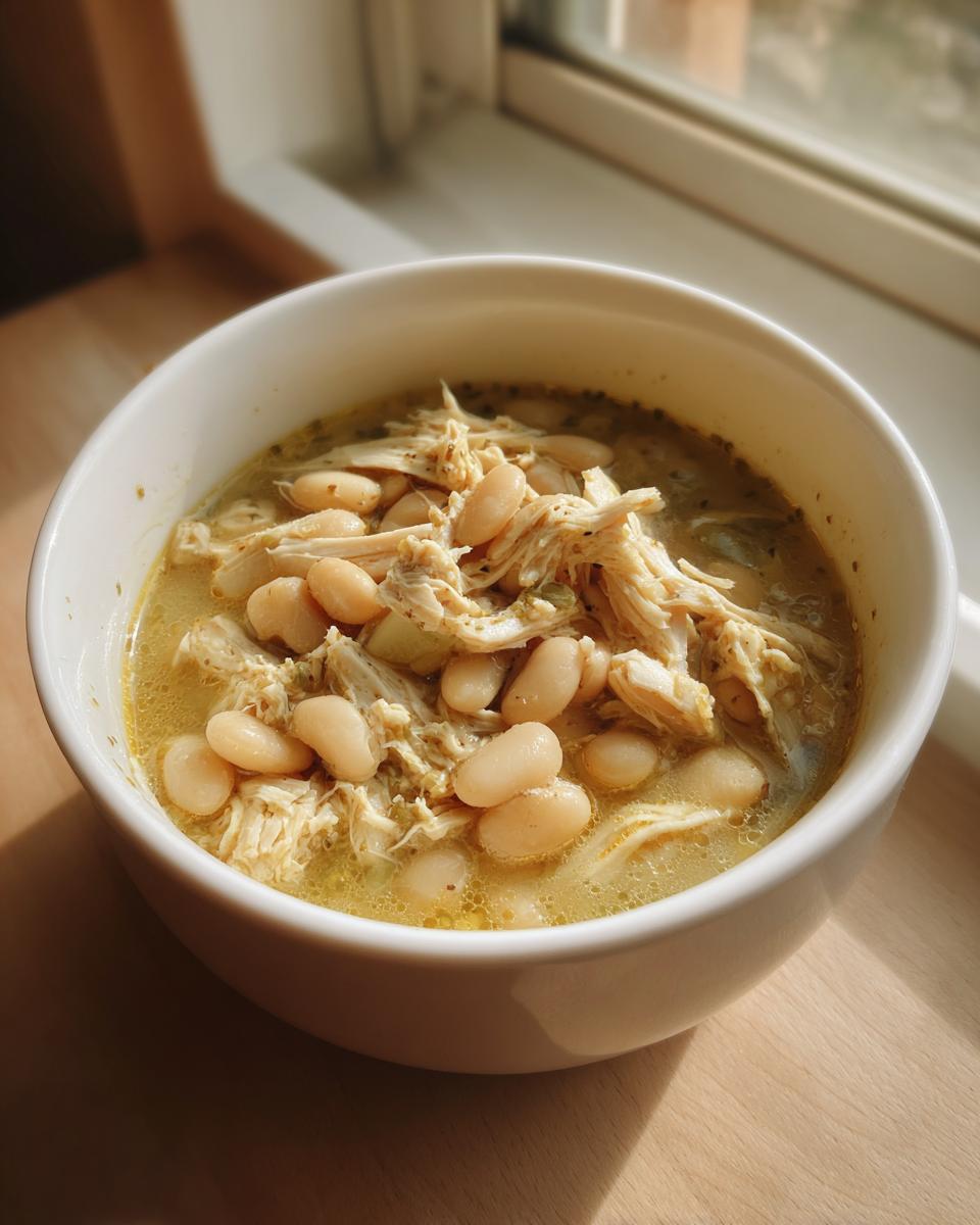 A close-up of a white bowl filled with hearty White Chicken Chili, featuring shredded chicken and white beans in a savory broth.