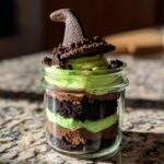 A layered Witch Halloween Cake Jar featuring chocolate cake, green frosting, and topped with a chocolate witch hat.