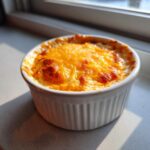 Close-up of freshly baked Buffalo Chicken Dip topped with melted, browned cheddar cheese in a white ramekin.