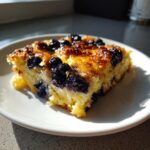 A close-up of a golden slice of Blueberry Buttermilk Pancake Casserole topped with baked blueberries.