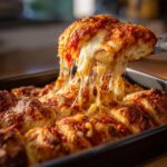 A piece of cheesy Pull Apart Pizza Bread is being lifted from the pan, showing long, dramatic cheese pulls.