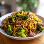 A close-up of a white bowl filled with savory Chicken Ramen Stir Fry mixed with tender chicken pieces and bright green broccoli florets.