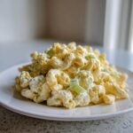 A close-up of a mound of creamy American Macaroni Salad, featuring elbow macaroni coated in dressing with visible celery pieces.