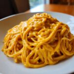 Close-up of spaghetti noodles generously coated in a rich, vibrant orange Butternut Squash Pasta Sauce on a white plate.