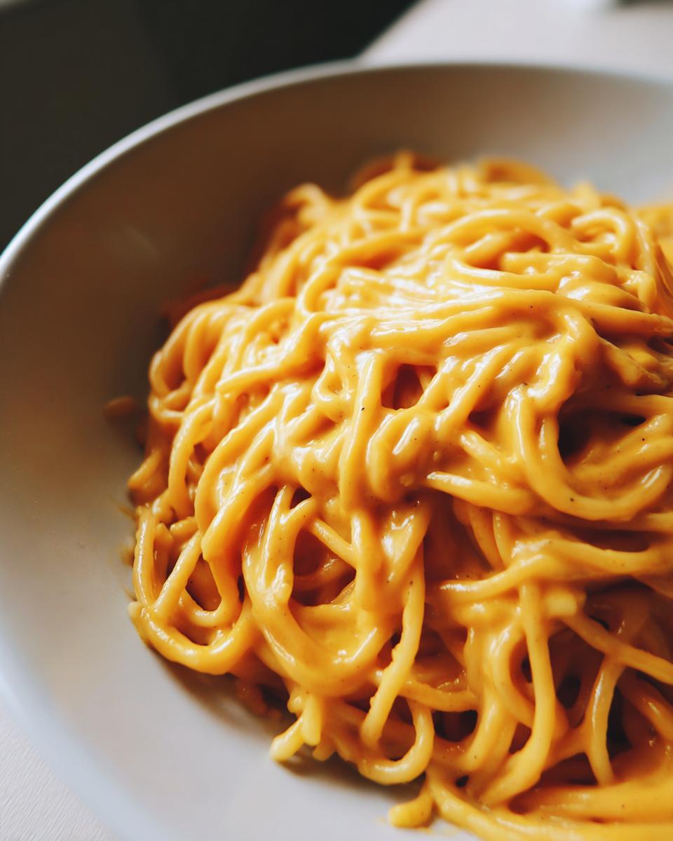 Close-up of spaghetti noodles coated thickly in a rich, orange Butternut Squash Pasta Sauce in a light bowl.