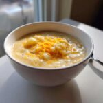 A white bowl filled with creamy Crack Potato Soup, topped with shredded cheddar cheese and black pepper.