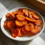 A plate piled high with bright orange, slightly charred Crispy Smashed Carrots seasoned with dark herbs.
