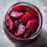 Overhead view of sliced Pickled Beets submerged in dark red brine inside a clear glass jar.