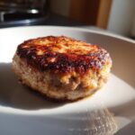 Close-up of a perfectly seared, juicy Turkey Burger patty with a dark brown crust resting on a white plate.