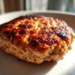 Close-up of a perfectly seared, juicy Turkey Burger patty with a rich brown crust resting on a white plate.