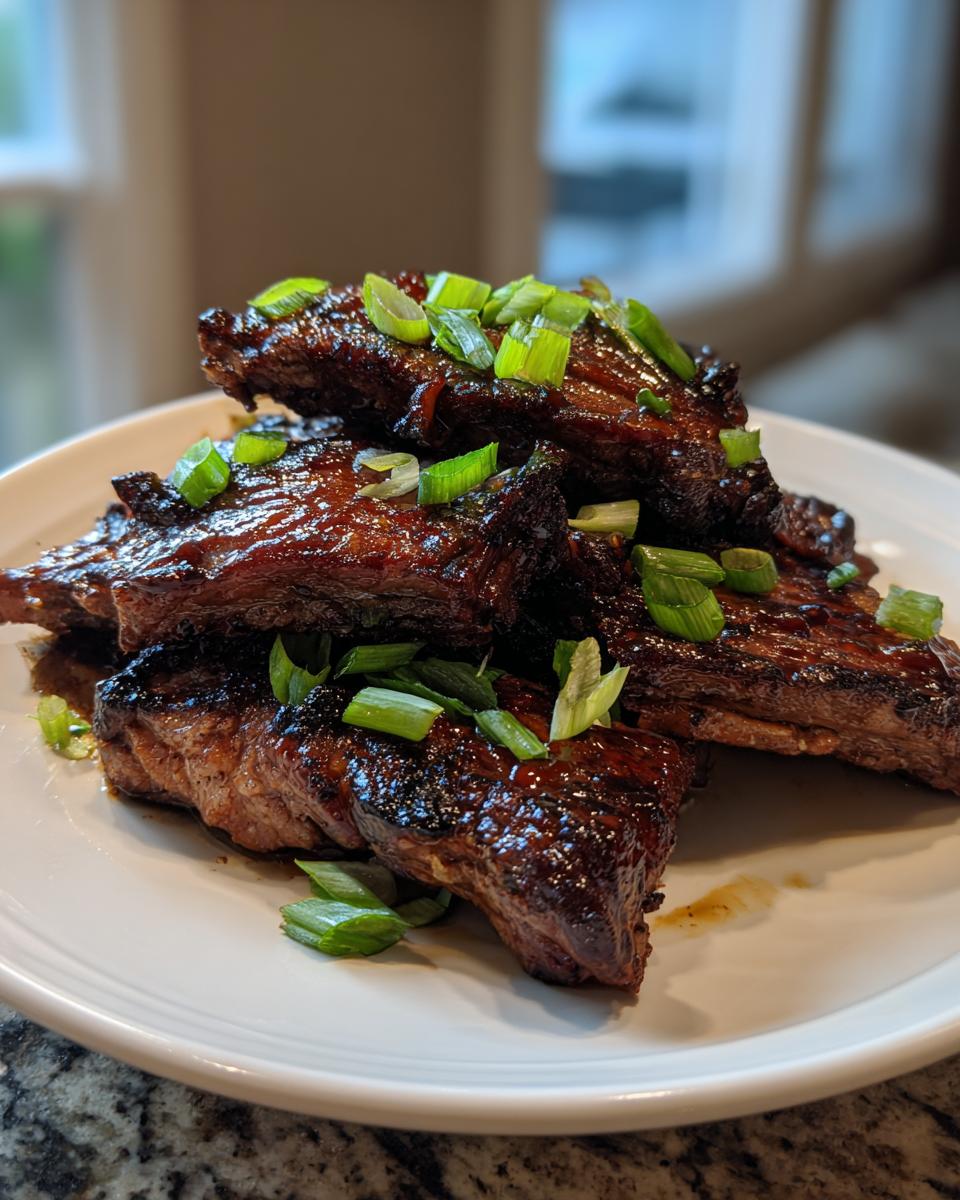 A stack of glossy, caramelized Korean Short Ribs garnished generously with freshly sliced green onions on a white plate.