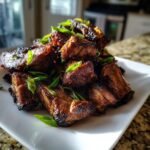 A pile of caramelized, glazed Korean Short Ribs garnished with fresh sliced green onions on a white plate.