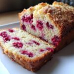 Close-up of a sliced loaf of moist Raspberry Bread showing bright red fruit baked into the crumb.