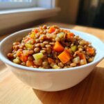 A white bowl filled with savory One Pot Lentils mixed with diced carrots and celery, brightly lit.