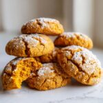 A stack of soft, cracked Pumpkin Spice Cookies dusted generously with powdered sugar, one cookie is broken open showing the soft interior.