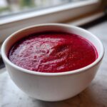 Close-up of a bowl filled with vibrant, deep red Spiced Cranberry Soup, lightly seasoned with pepper.