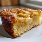 A close-up of a moist slice of Swedish Apple Cake topped with caramelized, glazed apple slices.