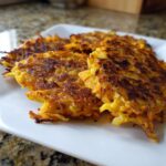 Four golden-brown, crispy Sweet Potato Apple Hash Browns piled on a white square plate.