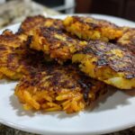 A close-up of several crispy, golden-brown Sweet Potato Apple Hash Browns stacked on a white plate.