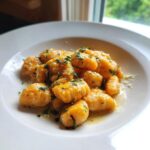 A close-up of bright orange Sweet Potato Gnocchi tossed in butter sauce and topped with fresh parsley.