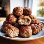 A close-up of a pile of perfectly browned Italian Meatballs, one cut in half showing the tender interior texture.